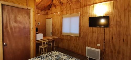 a room with a bed and a television on a wooden wall at Cabañas Trabun-Leufu in La Unión