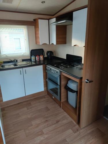 Il comprend une petite cuisine avec des placards blancs et une cuisinière. dans l'établissement Cairnryan Heights t-a Brae Holiday Homes, à Cairnryan