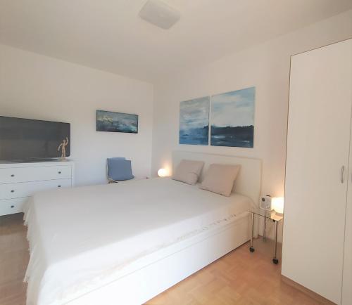 a white bedroom with a white bed and a tv at Ganze Wohnung am Wörthersee in Pörtschach am Wörthersee