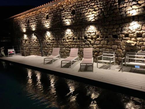 a group of chairs sitting on a dock next to a stone wall at CASARIOU Les Bernards Villa Grande bâtisse 12p avec cheminée bain nordique billiard piscine in Vaudevant