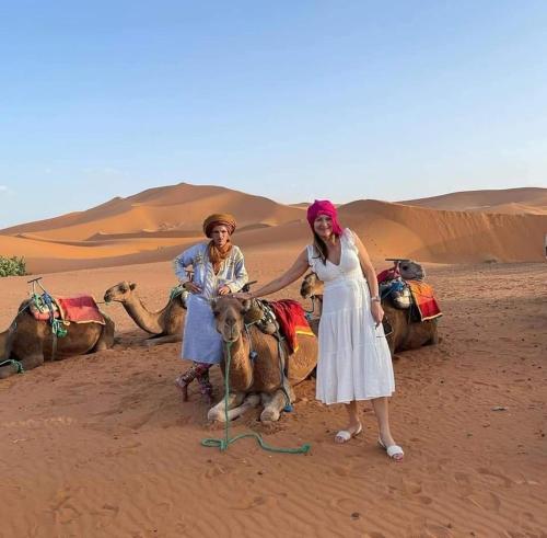 two women standing next to a camel in the desert at desert camp sahara luxury in Merzouga