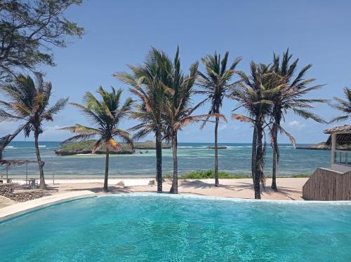 uma piscina ao lado de uma praia com palmeiras em Lily Palm Resort em Watamu