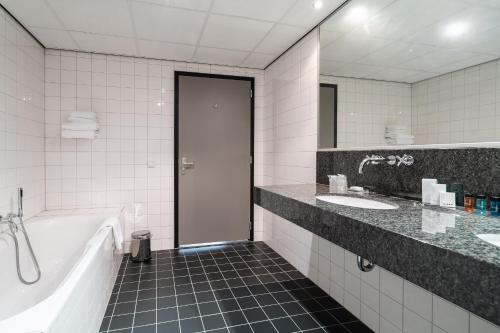 a bathroom with a tub and two sinks and a bath tub at Onderwijshotel De Rooi Pannen Eindhoven in Eindhoven