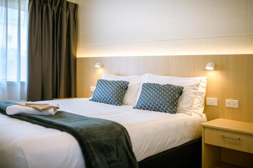 a hotel room with a bed with blue and white pillows at Takapuna International Motor Lodge in Auckland