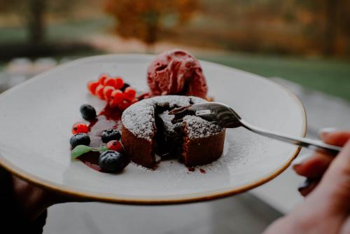 a person holding a plate with a piece of cake with a ice cream at Hanza Pałac Wellness & SPA in Warlubie