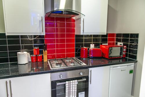 a kitchen with a stove and a red tiled wall at Meridian Serviced Apartments in Bradford