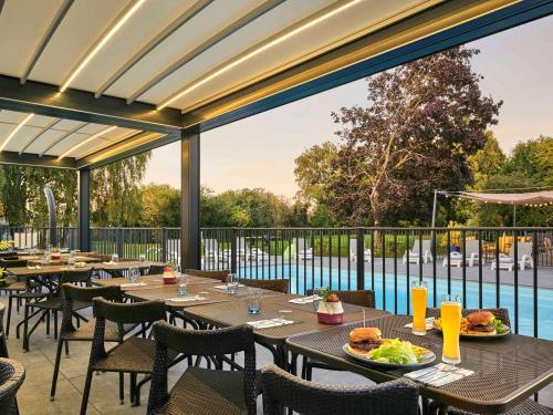 ein Restaurant mit Tischen und Stühlen und einem Pool in der Unterkunft Novotel Roissy Saint Witz in Saint-Witz