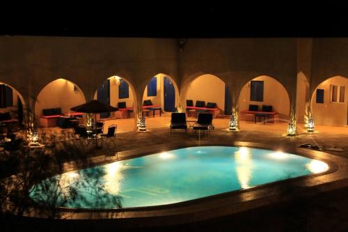 a large swimming pool in a building with chairs and tables at Hotel Riad Ali in Merzouga