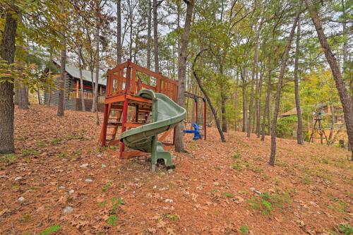 a playground in the woods with a slide at Tudor-Style Broken Bow Cottage with Hot Tub and Decks! in Stephens Gap