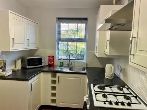 uma cozinha com armários brancos, um lavatório e um micro-ondas em Bullfinch House em Harleston