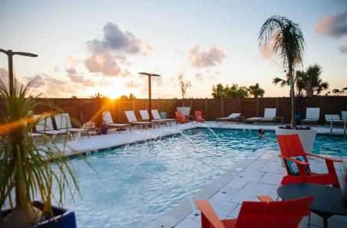 a pool with chairs and the sunset in the background at Hotel Indigo Orange Beach - Gulf Shores by IHG in Gulf Shores