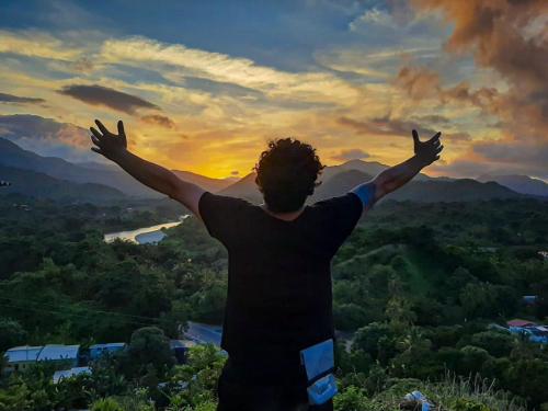 a man standing on top of a hill with his arms outstretched at Cristal Tayrona in Los Naranjos