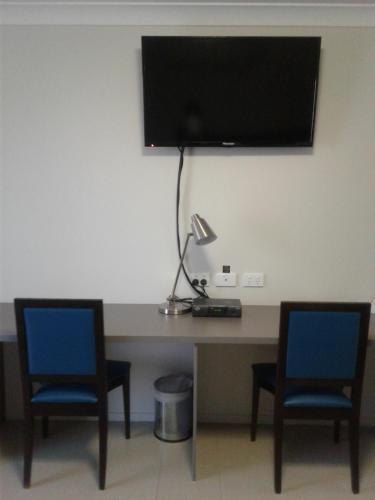 a desk with two chairs and a television on a wall at Royal Motel Miles in Miles