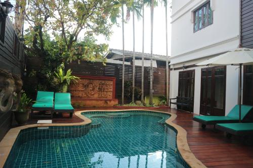 a swimming pool in the middle of a patio with green chairs at Rich Lanna House in Chiang Mai