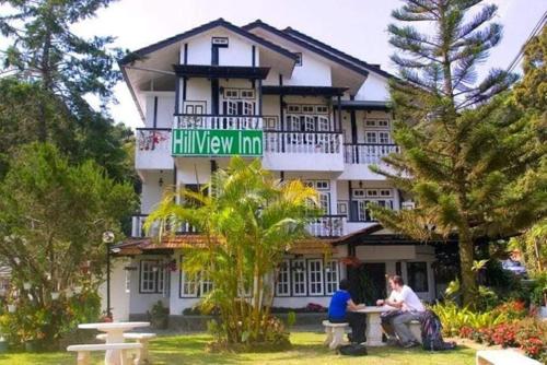 dos personas sentadas en una mesa frente a un edificio en Hillview Inn Cameron Highlands PROMO, en Tanah Rata