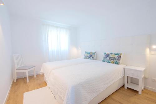 1 dormitorio blanco con 1 cama blanca y 1 silla en Penthouse with rooftop pool - Duna Parque Group, en Vila Nova de Milfontes