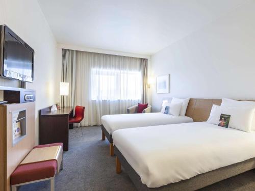 a hotel room with two beds and a television at Novotel Lens Noyelles in Noyelles-Godault