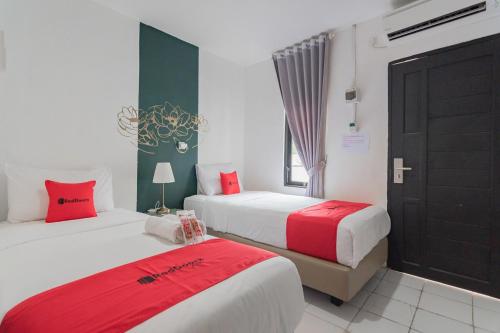two beds in a room with red and white at RedDoorz At Sani Guest House in Balikpapan