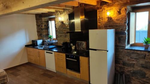 a kitchen with a white refrigerator and a stone wall at Casa Resineiro com Garagem e Terraço in Proença-a-Nova