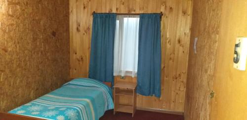 a small bedroom with a window with blue curtains at Hospedaje Picoyo in Pucón