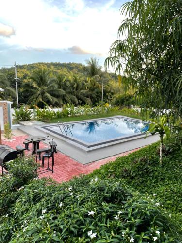 a pool with a table and chairs in a garden at Laura Guest House Langkawi in Pantai Cenang