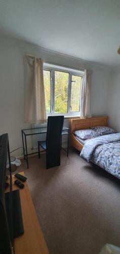 a bedroom with a bed and a desk and a window at Spacious and Serene Stay near Milton Keynes centre in Willen