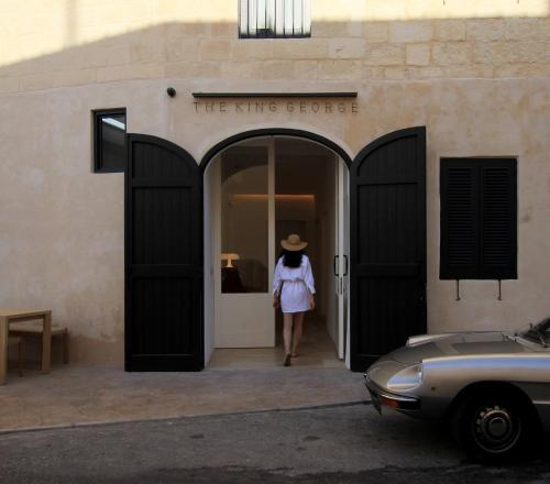 a woman in a hat walking out of a building at The King George Village Boutique Living in Għargħur