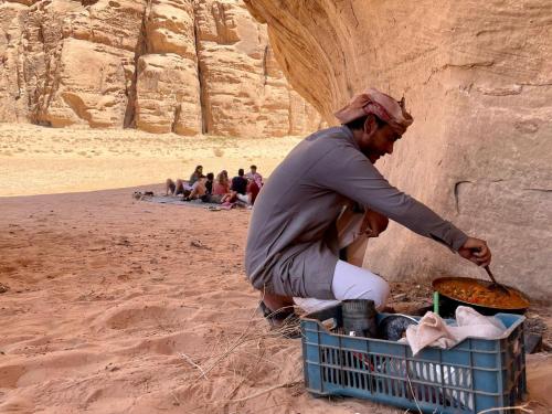 a man is cooking food in a basket in the desert at Wadi Rum Travel camp in Wadi Rum