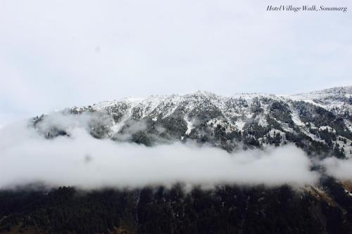 a mountain covered in snow and clouds at Hotel Village Walk in Sonāmarg