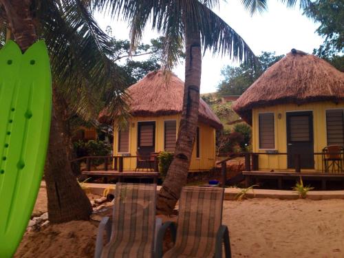 two chairs and a surfboard on a beach with two huts at Funky Fish Beach & Surf Resort in Malolo