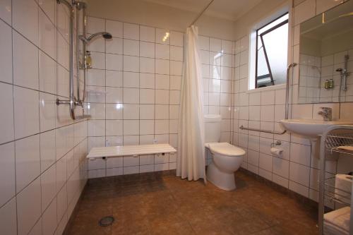 a white tiled bathroom with a toilet and a sink at 555 Motel Dunedin in Dunedin