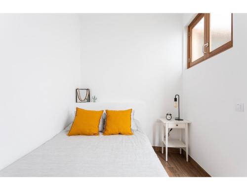 Una cama blanca con almohadas naranjas en una habitación blanca en La Casita de Juana, en Buenavista del Norte