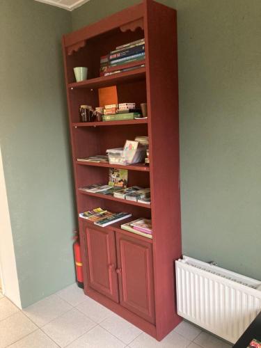 a red book shelf in a room with books at De Deelderij in Schoonloo