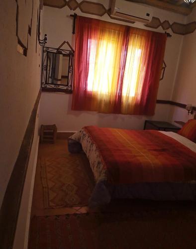 a bedroom with a bed and a window with a colorful blanket at Auberge des peupliers Café Restaurant in Akhendachou nʼAït Ouffi