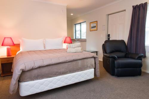 a bedroom with a bed and a black chair at Hamilton Settlers Motor lodge in Hamilton