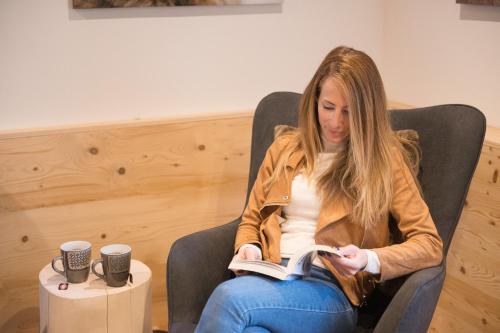 a woman sitting in a chair reading a book at Pimont Alpine Chalet in Madonna di Campiglio