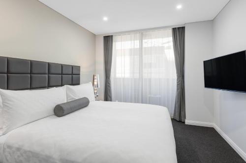 a bedroom with a white bed and a flat screen tv at Meriton Suites North Sydney in Sydney