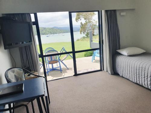 a room with a bed and a balcony with a television at Bay Vista Waterfront Motel in Picton