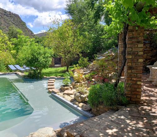 a swimming pool in a garden next to a house at De Poort Country Lodge in Oudtshoorn