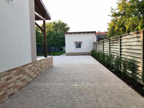 a brick driveway leading to a house with a fence at Vörösmarty apartmanház in Makó