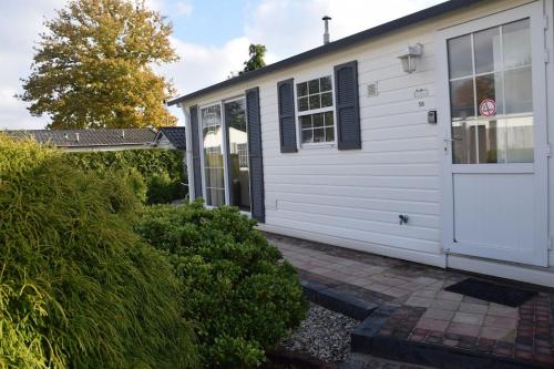 a white house with a white door and some bushes at Chalet Heggemus Oisterwijk in Oisterwijk