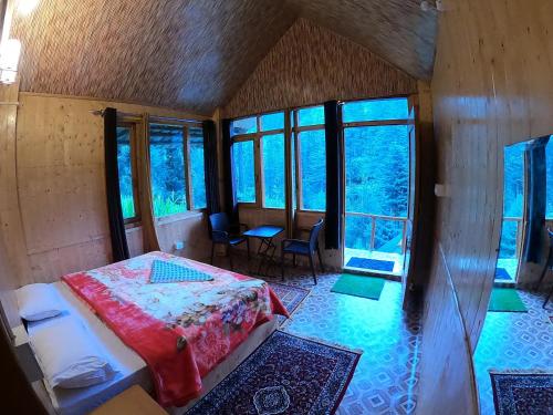 a bedroom with a bed in a room with windows at Reverberate Cafe & Cottages - Negi's Place in Jibhi