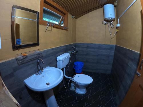 een badkamer met een wastafel, een toilet en een spiegel bij Reverberate Cafe & Cottages - Negi's Place in Jibhi