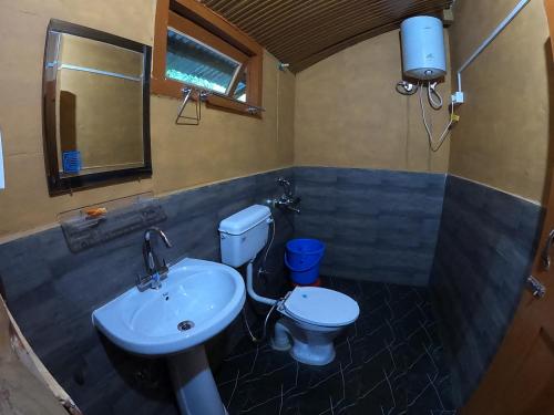 a bathroom with a sink and a toilet and a mirror at Reverberate Cafe & Cottages - Negi's Place in Jibhi