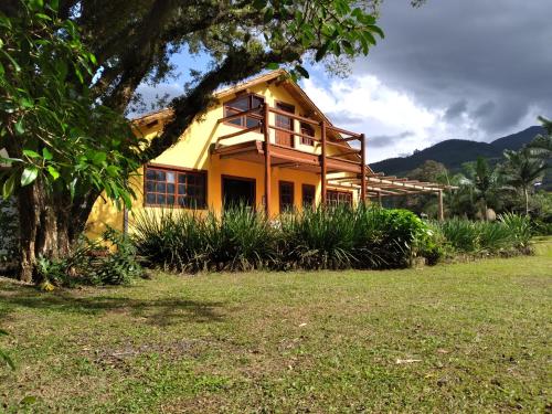 Una casa amarilla con un árbol delante. en Pousada Malacara, en Praia Grande