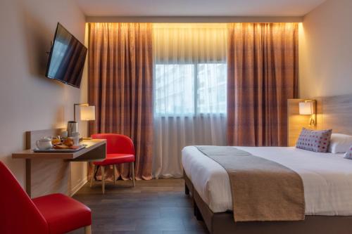 a hotel room with a bed and a window with a red chair at Hôtel L'Empreinte in Cagnes-sur-Mer