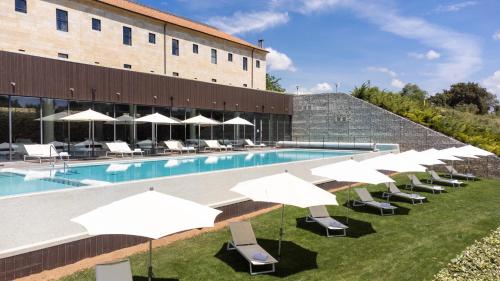 a pool with chairs and umbrellas next to a building at Castilla Termal Monasterio de Valbuena in Valbuena de Duero