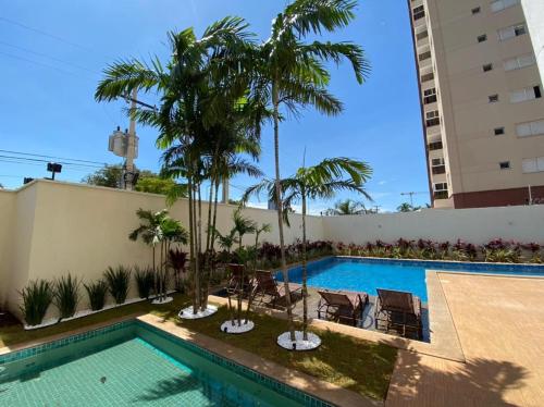 una piscina con palmeras junto a un edificio en PALMAS EXPERIENCE - APARTAMENTO CONTEMPORÂNEO, vista serra, próximo ao shopping en Palmas