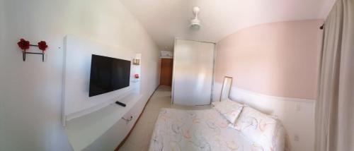 a white room with a bed and a flat screen tv at Verano Residencial in Guarajuba
