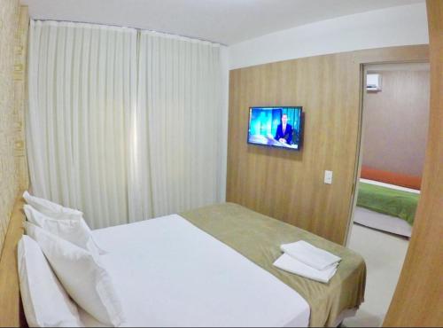 1 dormitorio con 1 cama blanca y TV en la pared en VG FUN-OCEAN VIEW BEACH FRONT APARTMENT-Fortaleza en Fortaleza
